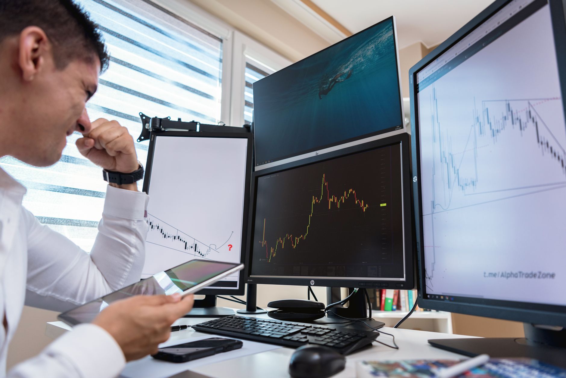 Trader compara diferentes gráficos de mercado exibidos em quatro monitores