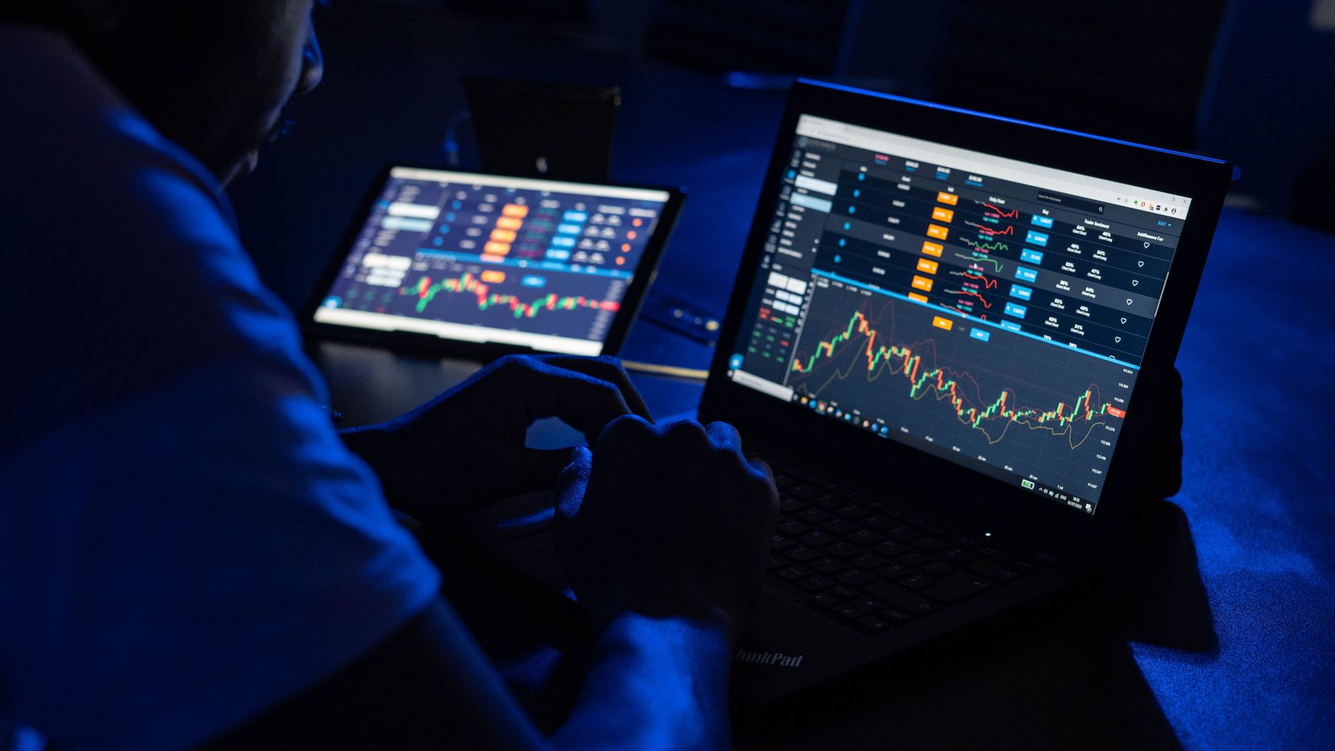 Trader acompanha gráficos em dois computadores numa sala com pouca luz
